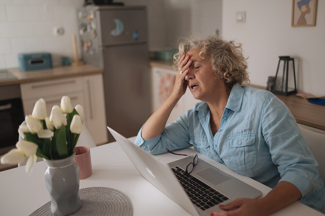 A woman at a laptop, rubbing her forehead